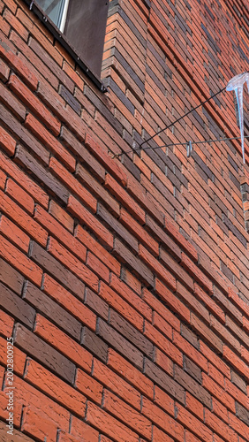 A close-up low angle view of a modern multi-colored red and brown brick wall facade with a sharp frozen icicle hanging from a wire during winter season