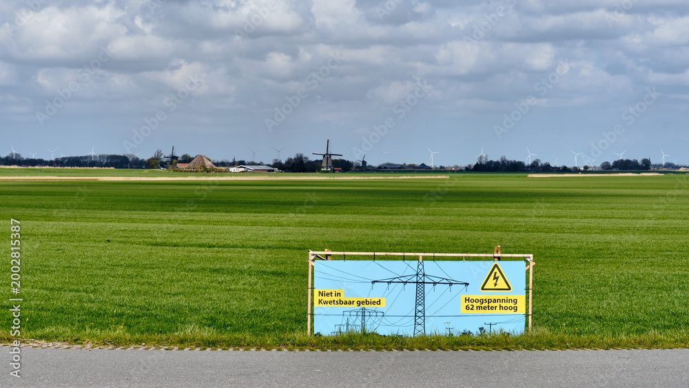 Obraz premium Protest Against High Voltage Power Lines In Rural Obdam Netherlands With Warning Sign And Windmills In Green Fields Energy infrastructure and rural development concerns showing a warning sign