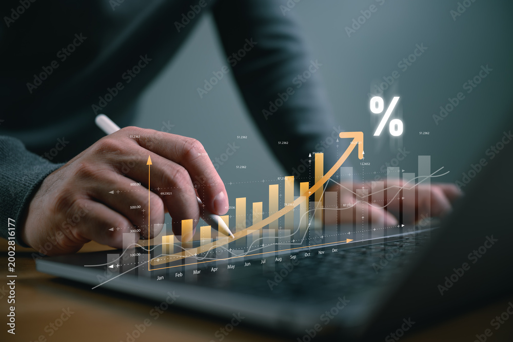 Naklejka premium Businessman hand using stylus pen on laptop with glowing rising growth graph and percentage icon. Concept of business success, financial profit, interest rate increase, and data analysis.