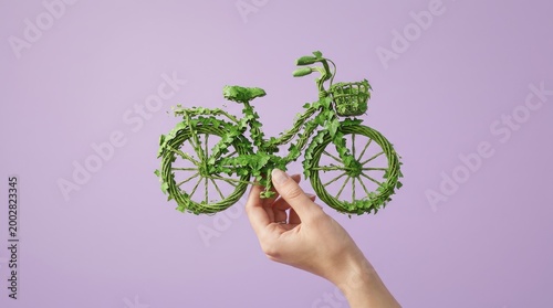 A hand holds a green bicycle made of leaves against purple background