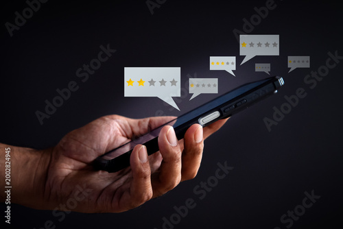 Obraz na płótnie A hand holds a smartphone displaying low star rating bubbles on a dark background