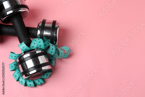 Foto Stylish dumbbells, measuring tape and rubber band on pink background