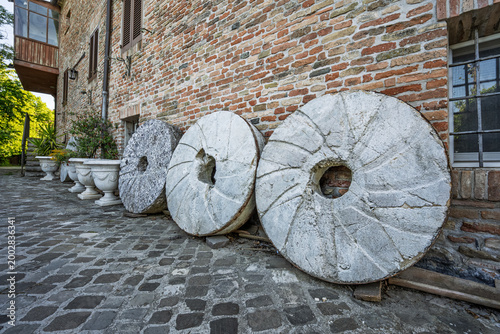 Photos Old stone millstones displayed against a rustic wall in the village of Mondaino,