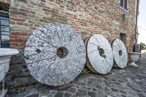 Bild auf Leinwand Old stone millstones displayed against a rustic wall in the village of Mondaino,