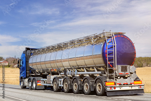 Blue Truck Shiny Tank Semi-Trailer at Speed on Road, Rear View. 