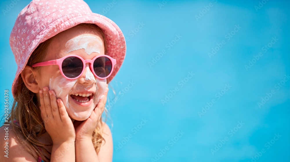 Fototapeta Happy child with sunscreen on face wearing sunglasses and hat outdoors