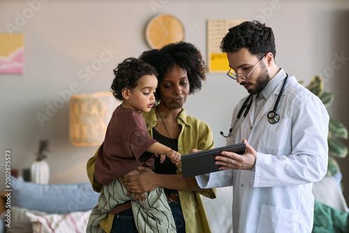 Tableau sur toile African American mother holding child while doctor showing tablet during home vi
