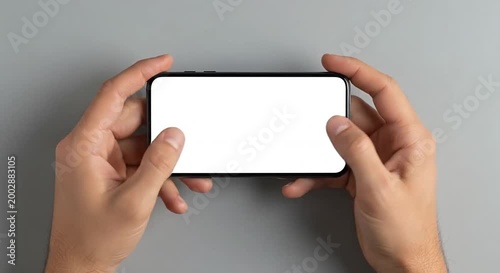Hands holding a smartphone horizontally with a blank white screen against a gray background