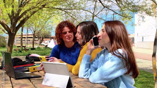 University students talking and studying together in a park using laptops and tablets