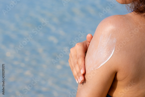 Fotografie Sunscreen from blue bottle on palm she apply hand and arm with bright sun and bl