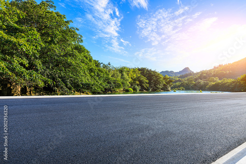 Empty asphalt road through green mountain forest under clear blue sky