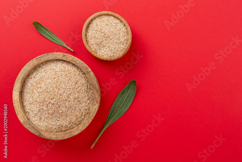 Fotografi Psyllium husk powder with fresh leaves on color background, top view