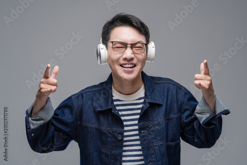 Cheerful Asian man wearing wireless headphones listening to music with eyes closed, happy male enjoying sound or podcast on grey background