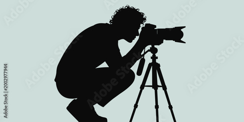 Silhouette of a creative freelance photographer crouching low with a professional DSLR camera mounted on a tripod, capturing a unique angle, possibly for nature, wildlife, event coverage, or street ph