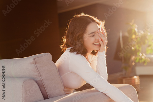 Quadro su tela Young woman laughing on a sofa in warm sunlight at home, relaxed and joyful mome
