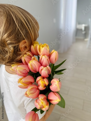 Cute little boy from behind with big bouquet of beautiful flowers tulips at home background. Child congratulation to Happy Mother's`s Day. International Women`s Day. Children and flowers.