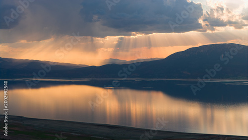 Beams of divine light filtering through the clouds at sunset over Lake Burdur. The golden silhouette of the mountains reflected on the water.