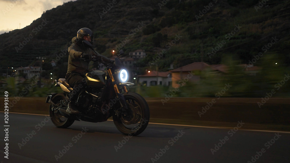 Fototapeta premium Biker riding motorcycle on mountain road during dusk