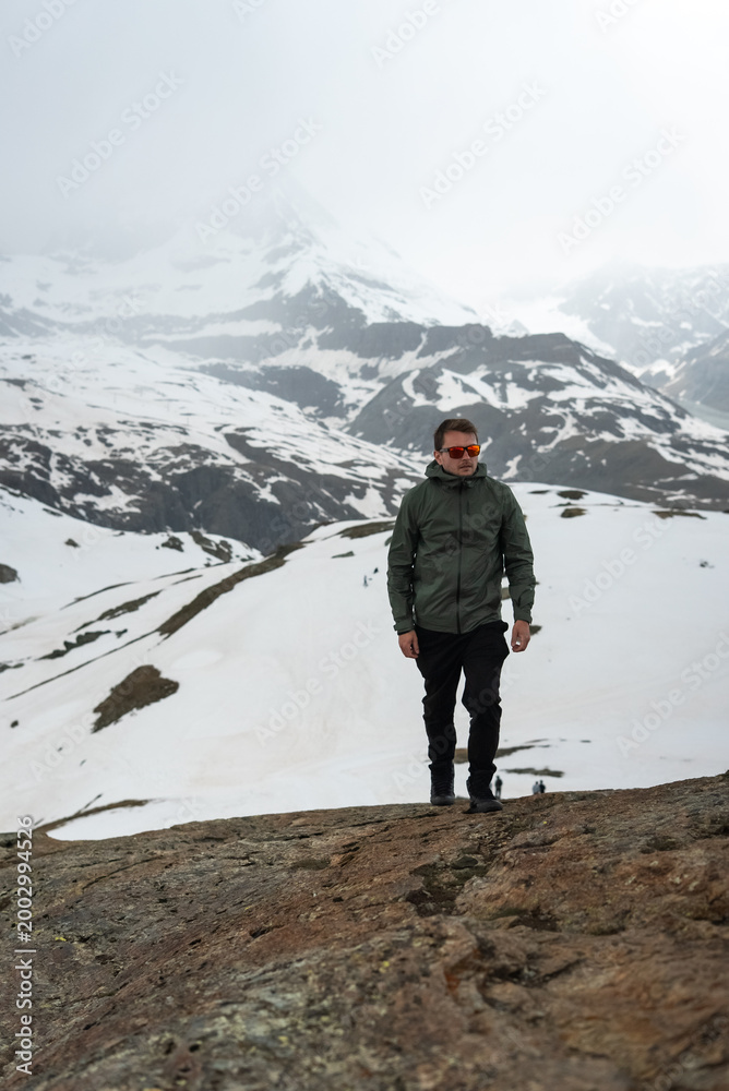 Obraz premium Man hiking rocky terrain with snow-capped mountain backdrop