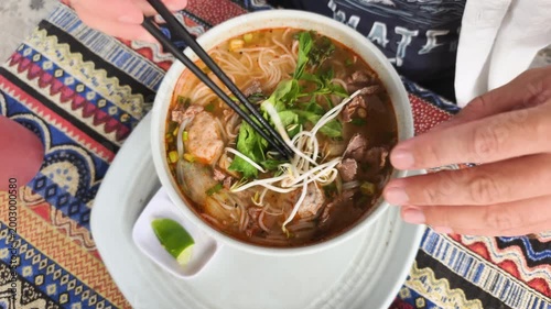 Fresh garnish for soup features hands adding green herbs and bean sprouts to hot broth. Vibrant mint and cilantro enhance aromatic Vietnamese noodle bowl. This fresh garnish for soup adds.