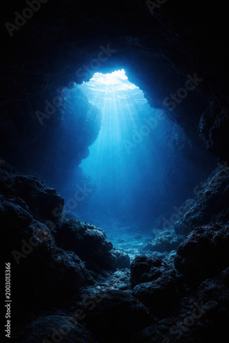 Underwater cave opening with blue light rays and dark ocean atmosphere