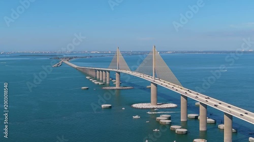 Cinematic drone shot of the iconic Sunshine Skyway Bridge spanning the turquoise waters of Tampa Bay on a bright, sunny day.