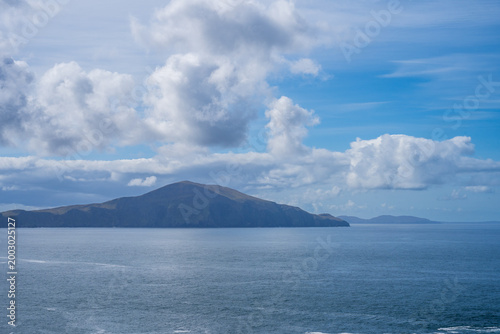 Canvastavla Island rises from calm Atlantic water beneath towering white clouds