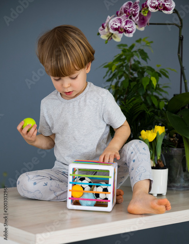 Little boy playing with sensory cube toy with colorful balls at home indoors. Baby activity cube with elastic bands. Motor skills development. Education and fun learning for modern children.