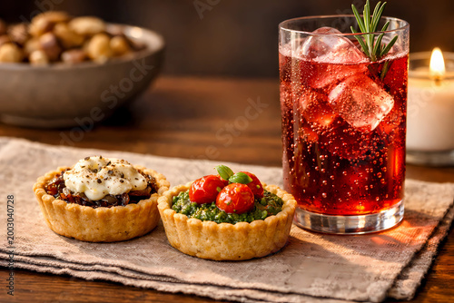 Mini savory tartlets with goat cheese and pesto next to a ruby-red sparkling non-alcoholic spritz. Bubbles, candlelight. Stock photo.