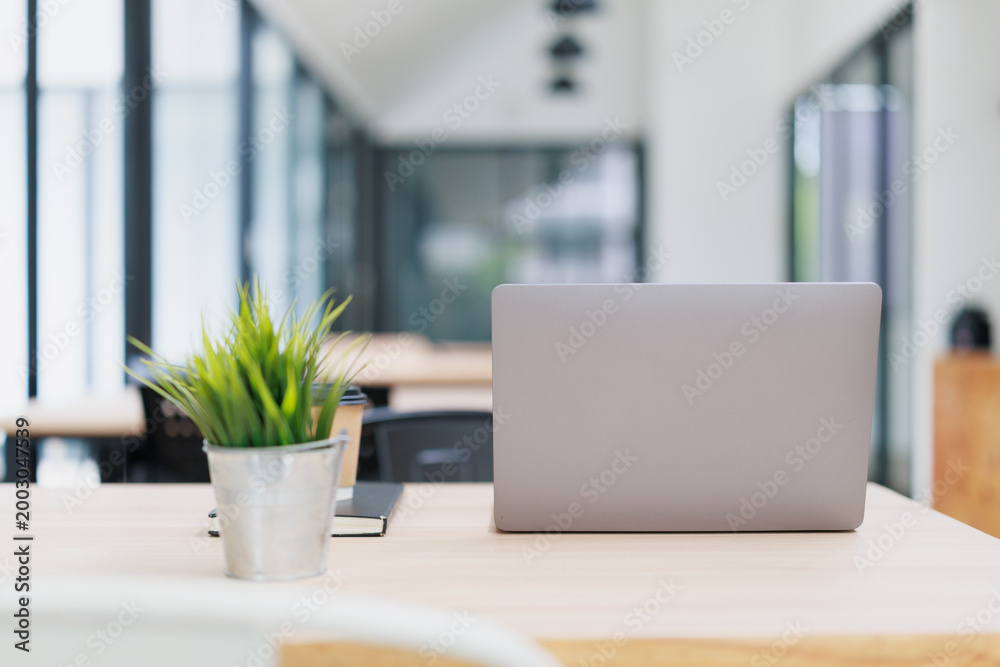 Fototapeta premium Employee working remotely at a modern office coworking space, desk with laptop, coffee, notebook, and a small plant, concept of freelance and business