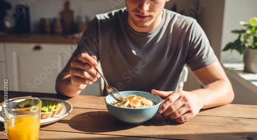 young adult gently stirring a spoon in a bowl of oatmeal at a sunlit kitchen table, simple morning breakfast moment.