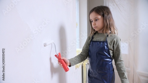 Fotografía Young girl in an apron painting an interior wall with a roller during a home ren