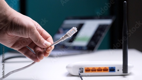 Картината върху платно Person's hand holding and connecting an ethernet cable to a white wireless route