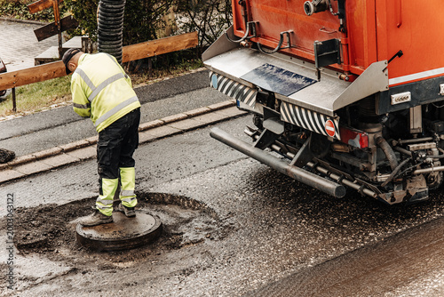 Bild auf Leinwand Worker Cleaning Manhole Cover During Road Maintenance and Asphalt Repair Project