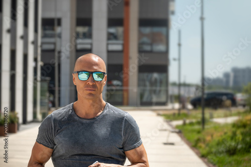 Handsome bald man in sunglasses outdoor, urban business success concept with leadership mindset, focus and determination, copy space