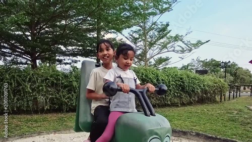 Two smiling little girls playing with a spring rider in an outdoor playground. Slow motion.