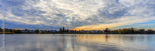 Sunset over river with clouds and trees in background, showing houses by water