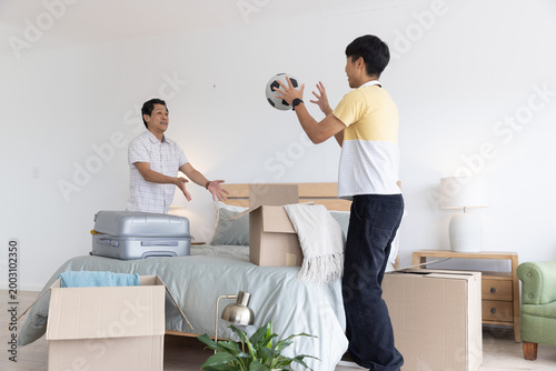 Bilde på lerret Asian men unpacking boxes in bedroom, passing black-and-white soccer ball near b