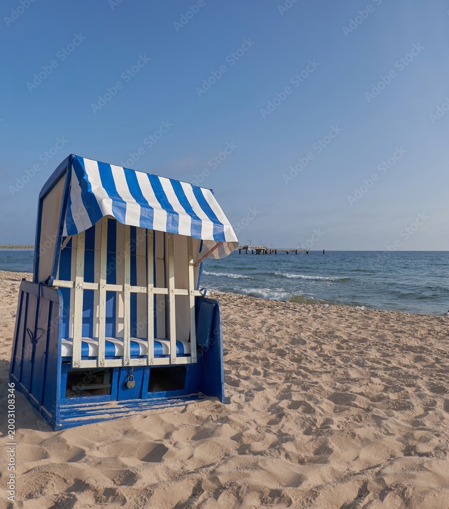 Fototapeta premium Strandkorb on sandy Rugen beach with blue striped canopy and calm Baltic Sea