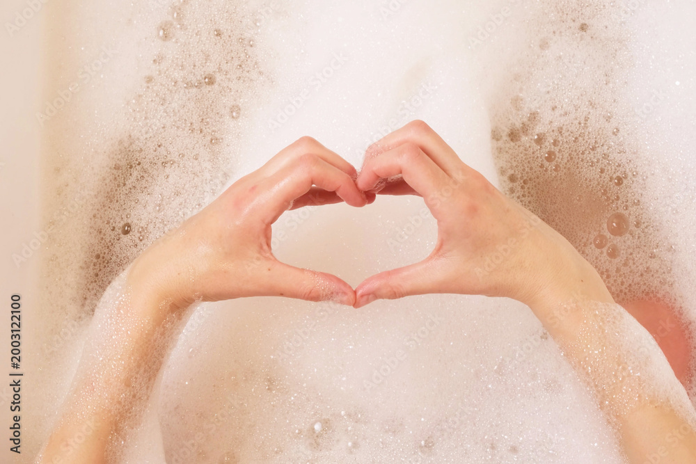 Fototapeta premium woman making heart shape with hands over bath foam
