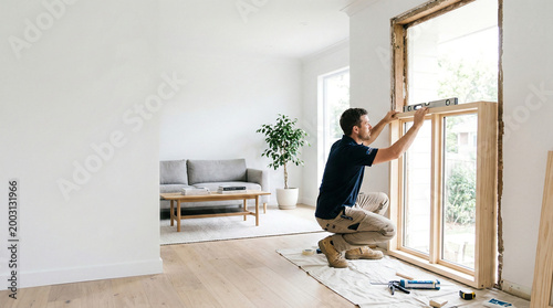 Professional carpenter installing new wooden window frame in a house.