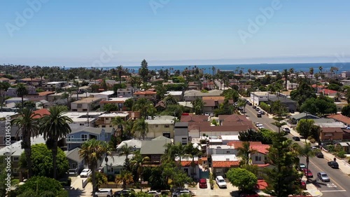 Drone rising above homes and palm trees in Ocean Beach San Diego moving toward the coastline and ocean.