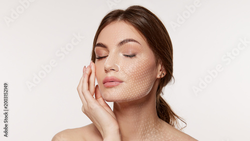 Foto Woman with closed eyes touches cheek as fine white facial mesh covers face and neck on clean background