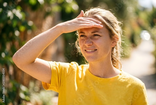 Young woman shielding eyes from bright sun outdoors