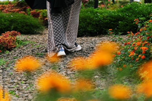 Low angle shot of a person walking on a gravel path in a garden, with blurry orange marigold flowers in the foreground for a creative perspective.