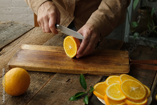 Hands slicing fresh oranges on wooden cutting board. Preparing citrus fruits for mulled wine or lemonade