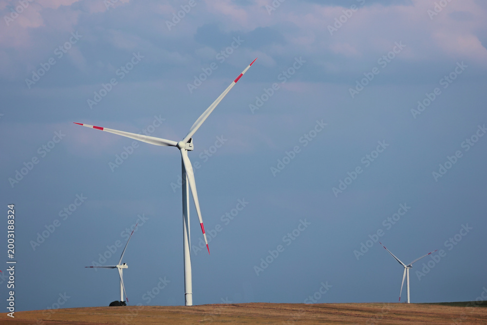 Fototapeta premium White wind turbines operating on a dry hill against a blue sky