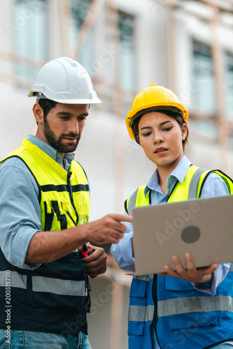 Obraz na plátne Construction worker team with hard hat and safety vest review plan on laptop at