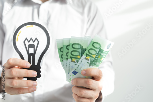 Person holding lightbulb and euro banknotes symbolizing financial gain from innovation and good idea