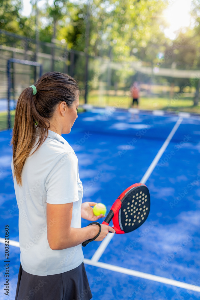 Fototapeta premium Woman holding padel racket and ball preparing to serve on outdoor court, calm moment before next rally in doubles match.